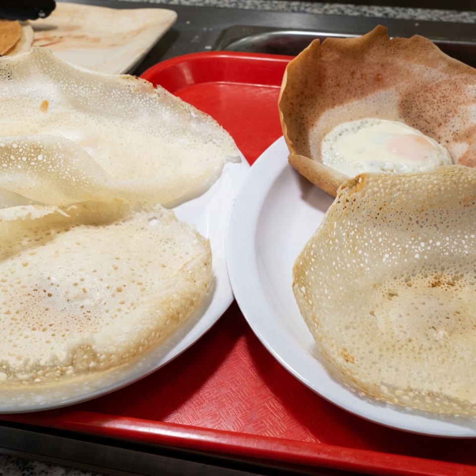 Four golden, lacy crepes served on white plates, with creamy sauce in one, arranged on a red cafeteria tray.